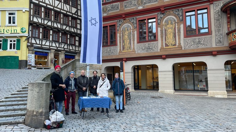 Sechs Menschen stehen vor einer gehissten Israel-Flagge. Im Hintergrund befindet sich das Tübinger Rathaus. Die sechs Mitglieder des Fördervereins für jüdische Kultur in Tübingen wollen dafür sorgen, dass die Israel-Flagge vor dem Rathaus diesmal hängen bleibt.