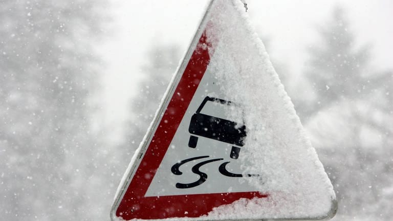 Ein schneebedecktes Verkehrsschild warnt vor Glätte.