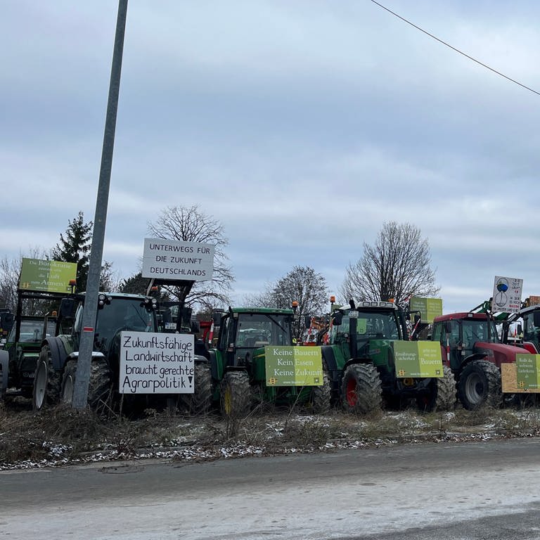 Mehrere Traktoren stehen an einer Straße geparkt. Sie präsentieren Plakate mit Sprüchen, die die Bundesregierung kritisieren.