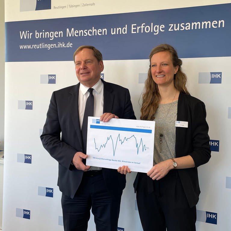 IHK-Hauptgeschäftsführer Wolfgang Epp und Antonia Hettinger, Leiterin regionale Wirtschaftspolitik halten ein Schaubild mit einer Konjunkturkurve in die Kamera. 