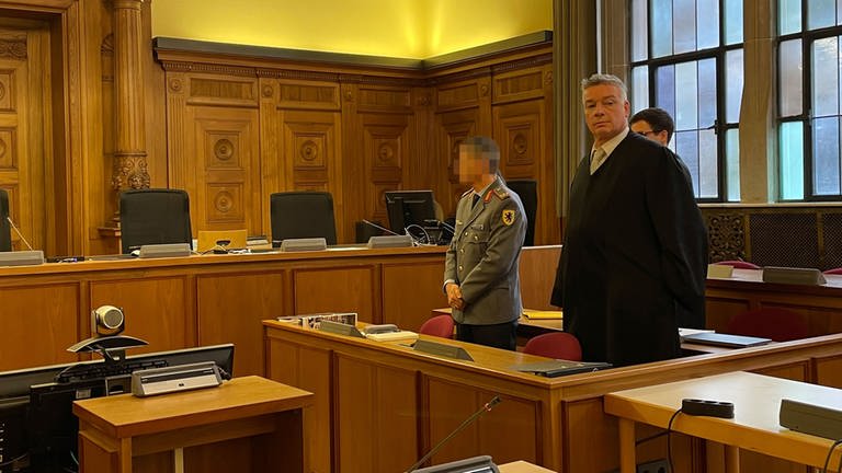 Ex-Brigadegeneral Markus Kreitmayr stehend im Gerichtssaal des Landgerichts Tübingen mit Blick auf den Richter. Rechts neben ihm sein Verteidiger Bernd Müssig, der in den Zuhörerbereich schaut.