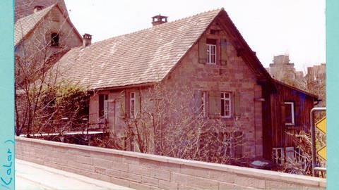 Man sieht eine Farbaufnahme der Rußhütte aus dem Jahr 1979. Damals gab es noch eine Brücke von der Straße zum Haus und mehrere Anbauten.