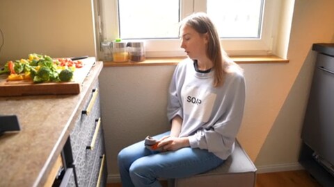 Anais Borrego sitzt auf einem Hocker in der Küche. Die Frau aus Balingen kämpft gegen Post-Vac. Die Booster Impfung veränderte ihr Leben. Nach der Pandemie fühlt sie sich immer noch im Stich gelassen. (Foto: SWR)