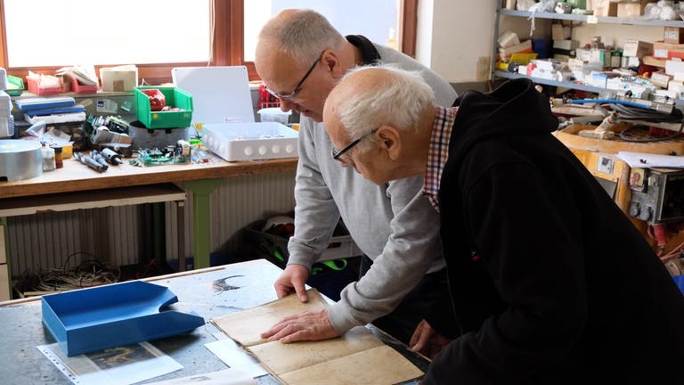 Andreas und Alfred Walz stehen in der Werkstatt und schauen sich alte Pläne der Kirchturmuhr an (Foto: SWR, Haas, Lisamarie)