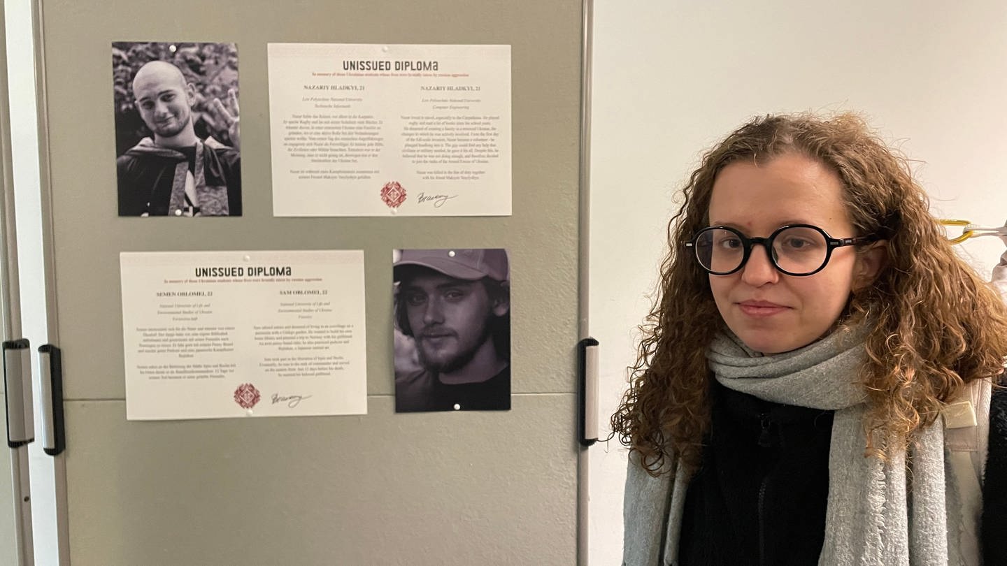 Junge Frau mit Brille neben einer Stellwand: Sie hat Studentinnen und Studenten in der Ukraine fotografiert, die später im Krieg gestorben sind. In Erinnerung an sie gibt es eine Ausstellung in Tübingen. (Foto: SWR, Peter Binder)