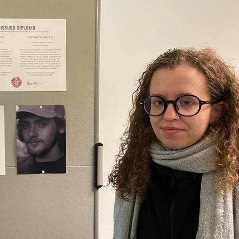 Junge Frau mit Brille neben einer Stellwand: Sie hat Studentinnen und Studenten in der Ukraine fotografiert, die später im Krieg gestorben sind. In Erinnerung an sie gibt es eine Ausstellung in Tübingen.