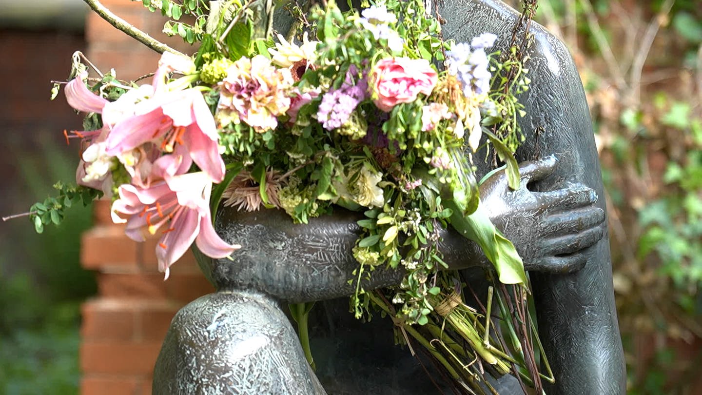 Man sieht einen Blumenstrauß im Arm einer Statue. (Foto: SWR)