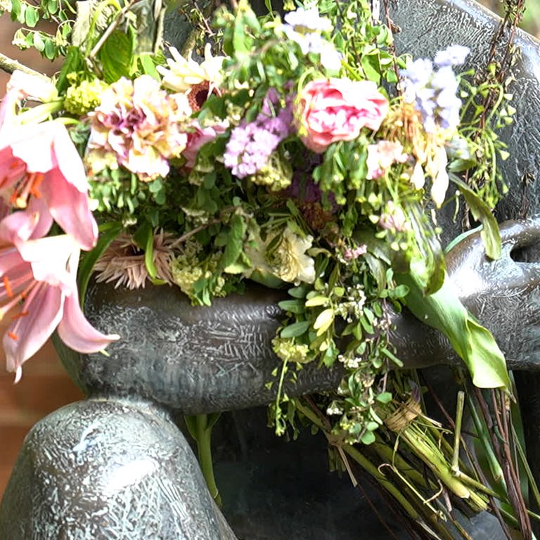 Man sieht einen Blumenstrauß im Arm einer Statue. (Foto: SWR)