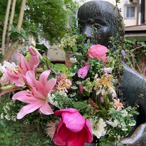 Man sieht eine Skulptur in einer Gasse in Tübingen. Sie hat einen großen Blumenstrauß in den Armen. Man nennt sie die "Sitzende". In Tübingen wundert man sich: Wer kümmert sich so liebevoll um die "Sitzende" und schenkt ihr Blumen?  (Foto: SWR)