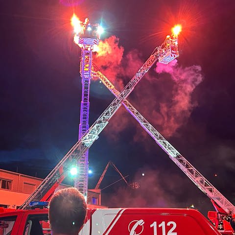 Brennende Fackeln tanzen auf ausgefahrenen Drehleitern bei der Nacht der offenen Tür der Feuerwehr Reutlingen. 