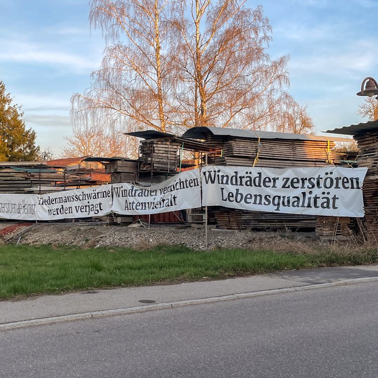 Ein Protestplakat gegen Windräder hängt neben einem Holzlager in Starzach, Kreis Tübingen. In Starzach wird ein Windpark mit sieben Windrädern geplant.