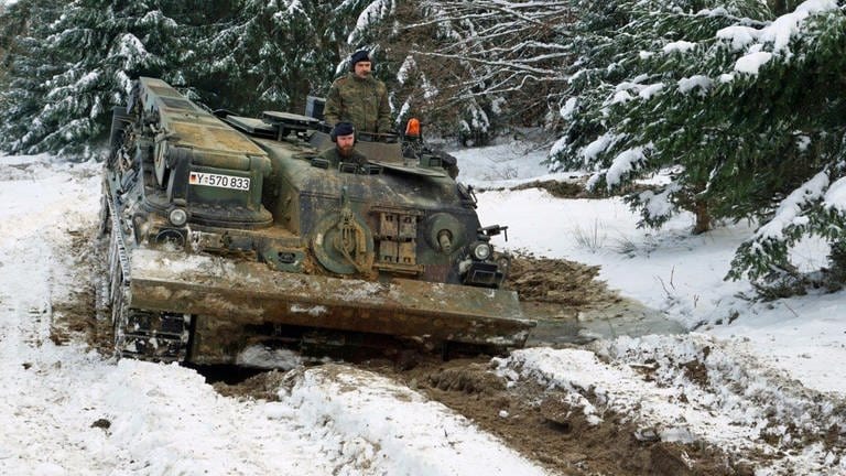 Ein Panzer mit zwei Soldaten rollt durch eine Kuhle aus Schnee und Matsch.