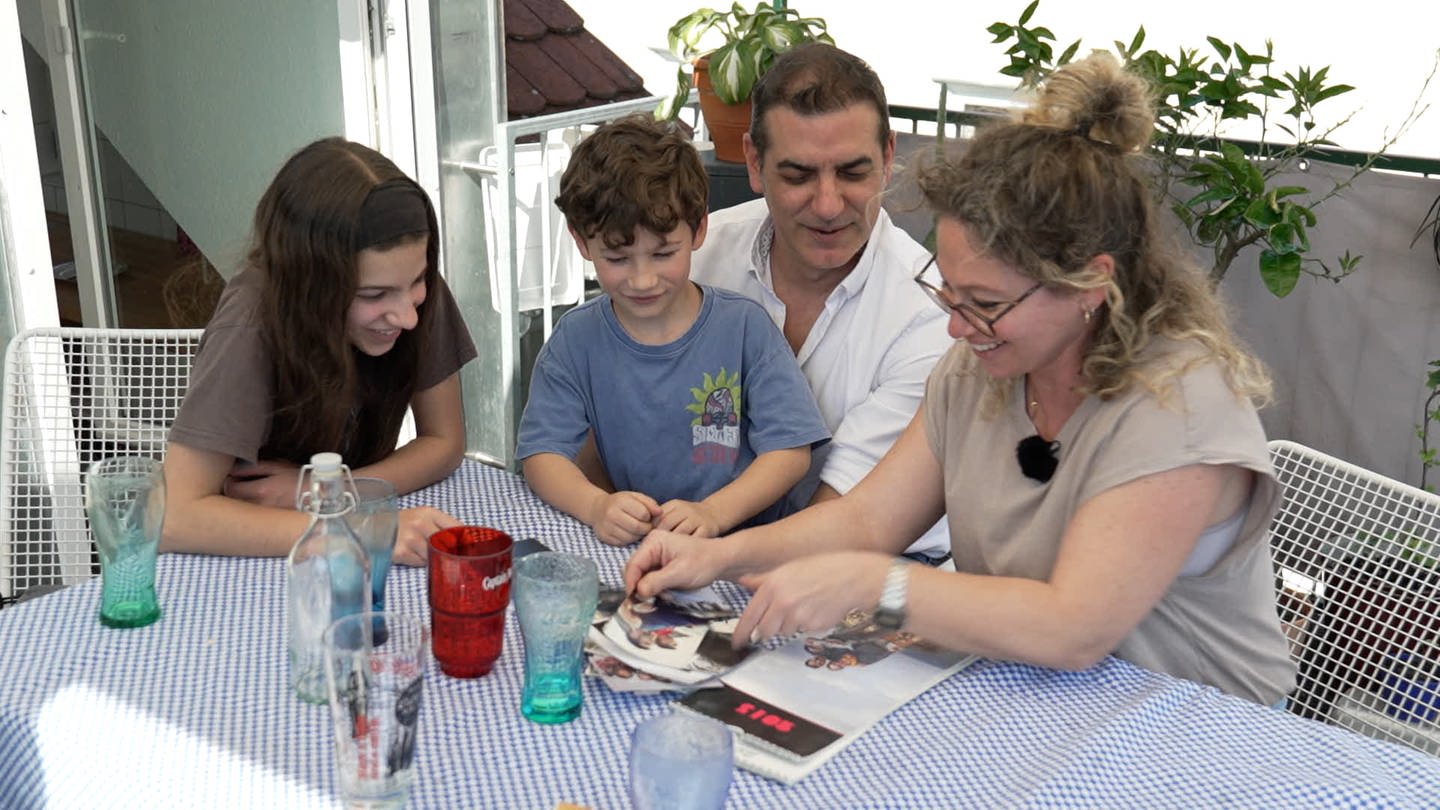 Die Familie Cardosa Zea / Markovic sitzt an einem Tisch auf dem Balkon und schaut Erinnerungsfotos an. Die Eltern haben sich bei einem Erasmus Semester kennengelernt (Foto: SWR, Nina Keppeler)