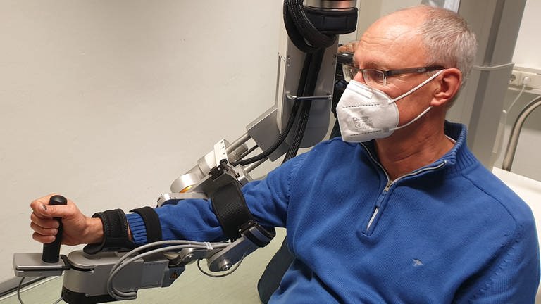 Eberhad Köhler ist als Testperson an einen Robotik angeschlossen, die seine Hand bewegt
