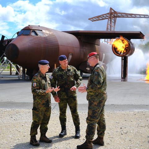 Bundeswehrsoldaten im Gespräch vor einem brennenden Flugzeug während einer Vorführung.