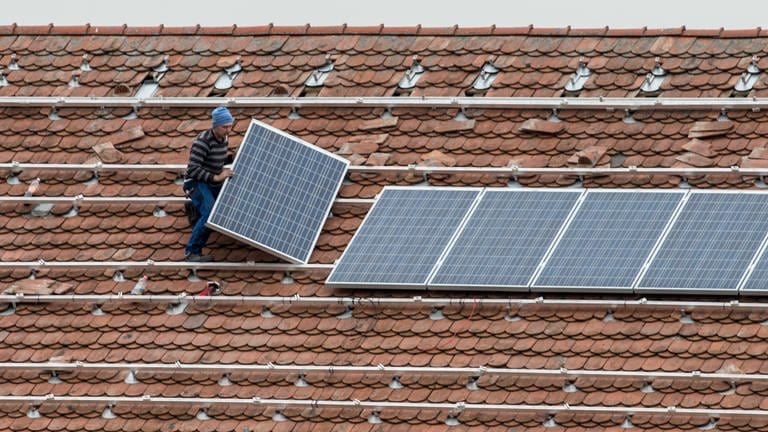 Mann bringt auf einem Dach Photovoltaikmodule an (Foto: dpa Bildfunk, Picture Alliance)