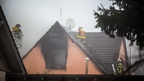 Ein Feuerwehrmann steht auf einem noch qualmenden Haus in Aalen und löscht einen Brand (Foto: Markus Brandhuber)