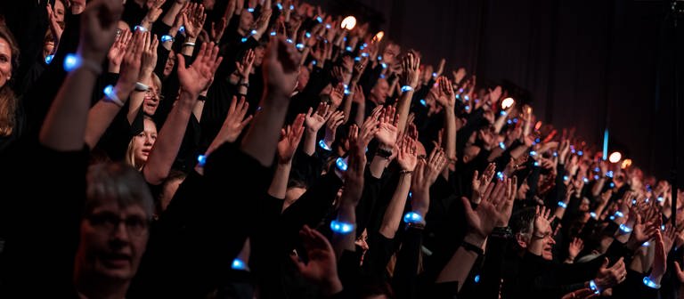 Sängerinnen und Sänger heben bei der Generalprobe des Chormusicals "Martin Luther King - Ein Traum verändert die Welt" ihre Arme in die Höhe (Foto: Stiftung Creative Kirche)