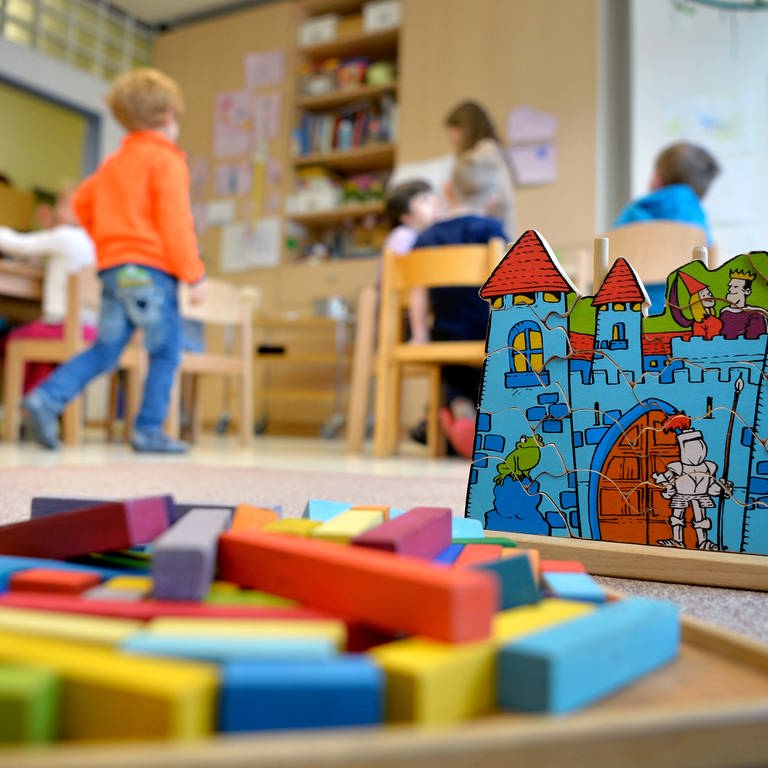 Spielzeug liegt in einem Kindergarten auf dem Boden, im Hintergrund sind spielende Kinder (Foto: dpa Bildfunk, picture alliance/dpa | Monika Skolimowska)