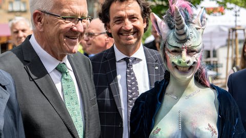 Schorndorf: Winfried Kretschmann, Ministerpräsident von Baden-Württemberg, steht neben einer bemalten Frau in Einhornmaske (Foto: dpa Bildfunk, picture alliance/Fabian Sommer/dpa)