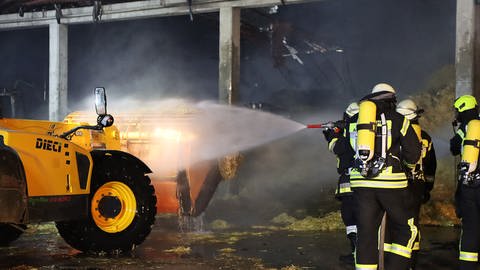Feuerwehrleute löschen vor einer ausgebrannten Halle einen Traktor. Beim Brand in einer Lagerhalle in Holzheim-Ellerbach wurde unter anderem eine Fotovoltaik-Anlage zerstört. (Foto: Mario Obeser)