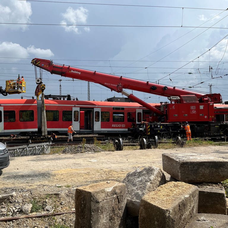 Ein roter Kran steht vor einem entgleisten Zug in einem Bahnhofsbereich. In Nördlingen hat die Deutsche Bahn begonnen, den entgleisten Regionalzug zu bergen.  (Foto: Tobias Hildebrandt)