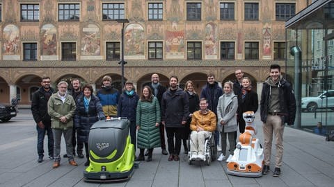 Gruppenbild mit Forscherteam und Servicerobotern: In Ulm soll getestet werden, wie Roboter und Menschen bei einer Begegnung im öffentlichen Raum miteinander zurechtkommen.  (Foto: Pressestelle, Stadt Ulm)