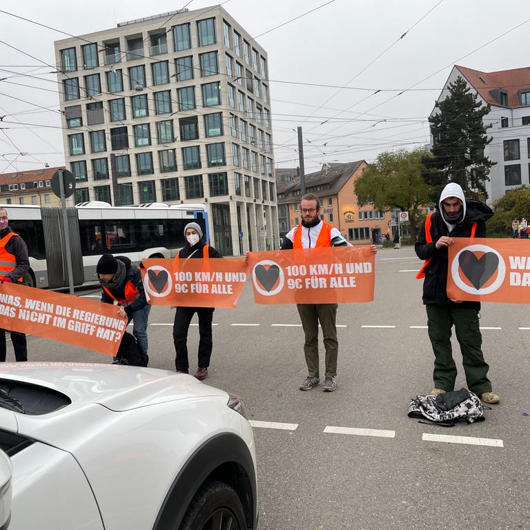 Klimaaktivisten blockieren mit Bannern Straße. In Ulm haben Aktivisten der Bewegung "Letzte Generation" sich dann auf der Fahrbahn festgeklebt.  (Foto: SWR, Catharina Straß)