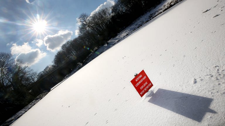 Ein eisbedeckter See an einem sonnigen Tag. Ein rotes Schild warnt davor, die Eisfläche zu betreten. Auch wenn die Temperaturen im Minusbereich bleiben. Die Wasserwacht warnt davor, jetzt schon auf das Eis zu gehen.  (Foto: dpa Bildfunk, picture alliancedpa  Roland Weihrauch)
