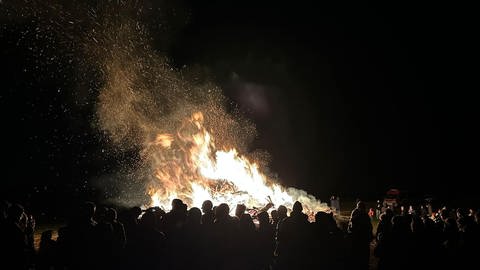 Flammen eines Funkenfeuers lodern in den Nachthimmel, davor eine Zuschauermenge. Das Funkenfeuer in Dietenheim-Regglisweiler (Alb-Donau-Kreis) war das bislang größte der Ortsgeschichte. (Foto: Raquel Koch Pérez)