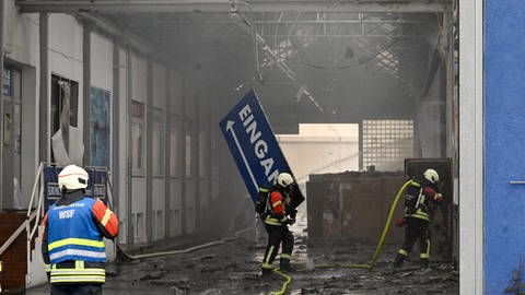 Feuerwehrleute im überdachten Zwischenteil der ausgebrannten Gebäude bei Jehle in Ulm. Nach dem Brand liegen Trümmer auf dem Boden, ein Eingangsschild hängt schief. Bei dem Großbrand ist ein Schaden von vier Millionen Euro entstanden. (Foto: Thomas Heckmann)
