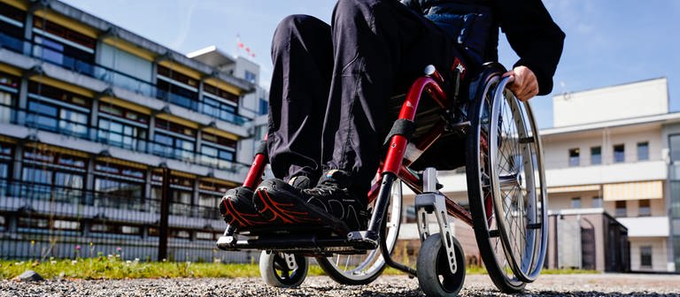 Ein Mann vor einem Klinikgebäude in einem Rollstuhl auf einem Kiesweg. Nach seiner Behandlung im Krankenhaus in Ehingen im Alb-Donau-Kreis hat ein Patient einen Rollstuhl geklaut. (Symbolbild) (Foto: dpa Bildfunk, picture alliance/dpa | Uwe Anspach (Symbolbild))
