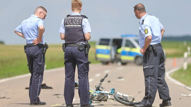 Polizisten schauen sich nach einem Unfall ein Kinderfahrrad auf der Straße an (Foto: z-media, Ralf Zwiebler)