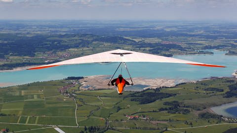 Ein weißer Drachen mit orangenem Innensegel - ein Drachenflieger schwebt in Richtung Forggensee über die Allgäuer Landschaft (Symbolbild).  (Foto: dpa Bildfunk, Karl-Josef Hildenbrand)