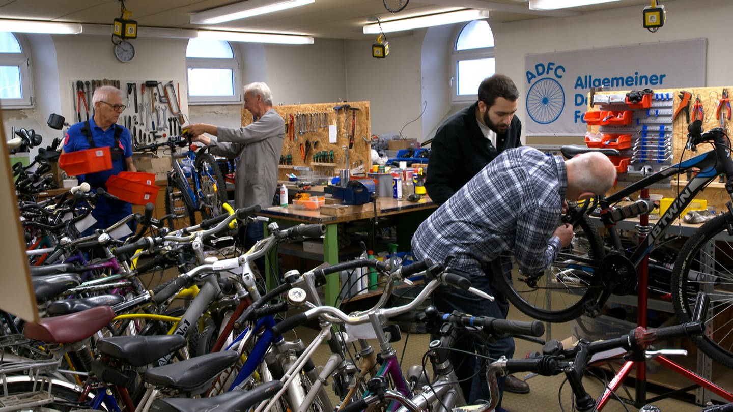 Einer der Schrauber der ADFC Werkstatt erklärt einem Austauschstudent der Hochschule Aalen, wie er ein Fahrrad reparieren kann. (Foto: SWR)