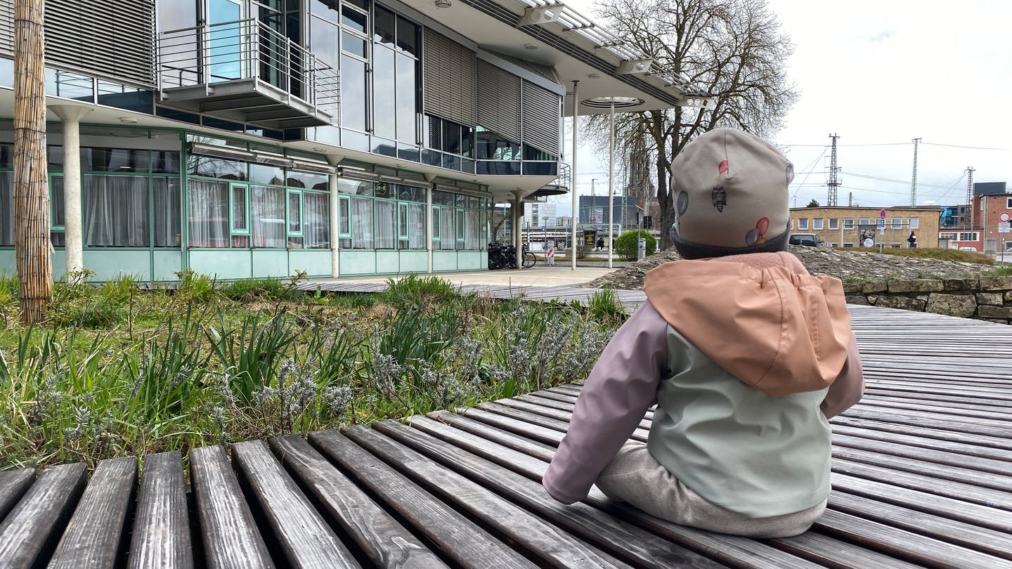 Das 9-Monate alte Pflegekind sitzt auf einer Bank vor dem Landratsamt des Alb-Donau-Kreises. (Foto: SWR, Maja Nötzel)