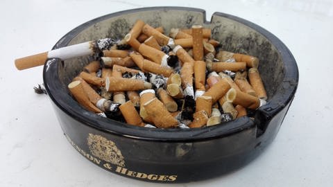 Ein voller Aschenbecher mit einer brennenden Zigarette