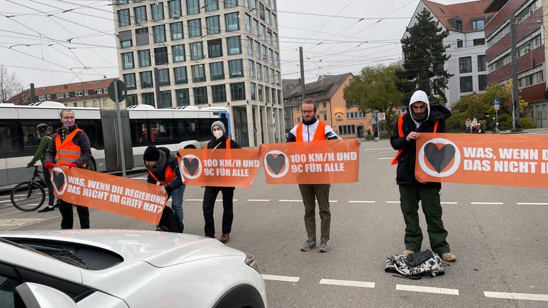 Klimaaktivisten blockieren mit Bannern Straße. In Ulm haben Aktivisten der Bewegung "Letzte Generation" sich dann auf der Fahrbahn festgeklebt.  (Foto: SWR, Catharina Straß)