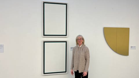 Stefanie Dathe steht vor zwei Gemälden, die fast komplett weiß sind. 