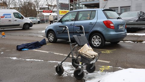 Unfall auf einer Straße mit beteiligtem Auto, einem Rollator und einer blauen, auf der Fahrbahn liegenden Decke. Ein 92-jähriger Fußgänger ist am Montagmittag in Ulm von einem 88-jährigen Autofahrer erfasst und schwer verletzt worden.  (Foto: z-media, Ralf  Zwiebler)