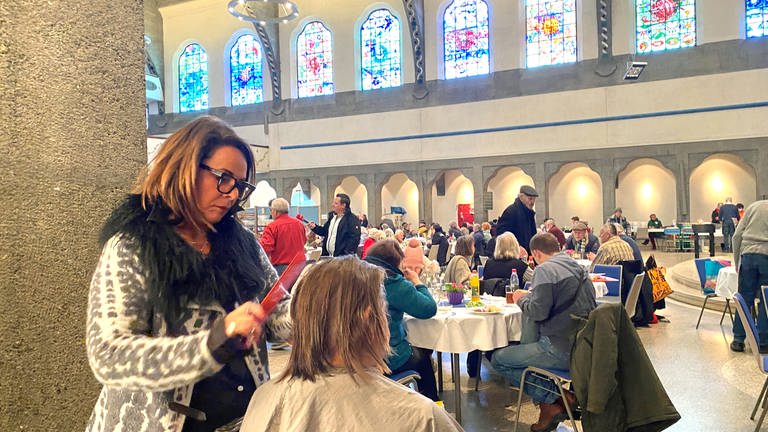 Eine Frau schneidet einer anderen in einer Kirche die Haare. Seit 20 Jahren schneidet Friseurmeisterin Maria Hartmann Gästen der Ulmer Vesperkirche kostenlos die Haare. 