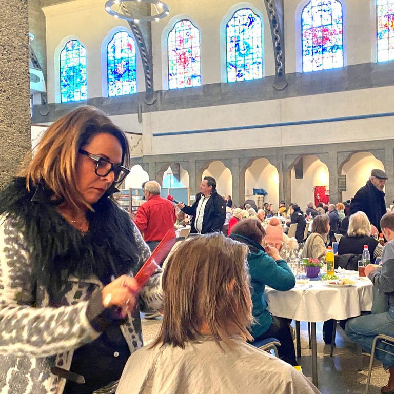 Eine Frau schneidet einer anderen in einer Kirche die Haare. Seit 20 Jahren schneidet Friseurmeisterin Maria Hartmann Gästen der Ulmer Vesperkirche kostenlos die Haare.  (Foto: SWR, Hannah Schulze)