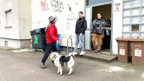 Ein Mann mit Hut und Hund vor dem Eingang zu einem Haus. Lemmy zeigt bei seiner Stadtführung den Studierenden auch das DRK-Übernachtungsheim für Wohnungslose in Ulm. (Foto: SWR, Hannah Schulze)
