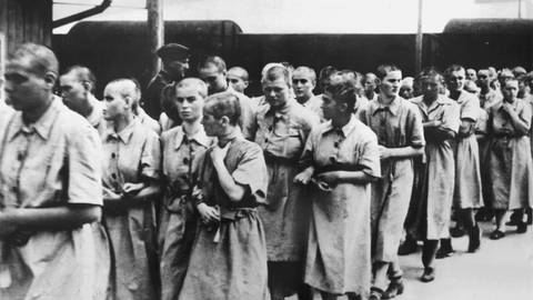 Frauen in Kitteln laufen in Reih und Glied. Weibliche Häftlinge des Konzentrationslagers Auschwitz werden zum Arbeitseinsatz im Reichsgebiet abtransportiert (undatiertes Archivbild). (Foto: dpa Bildfunk, Picture Alliance)