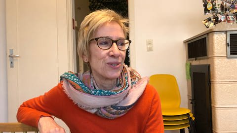 Eine Frau mit Brille und Schal sitzt am Tisch und lächelt. Christiane Blessing-Win vom Verein "Altersarmut Ulm nein e.V." (Foto: SWR)