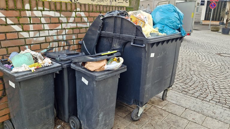 Mülltonnen stehen überfüllt an einer Hauswand