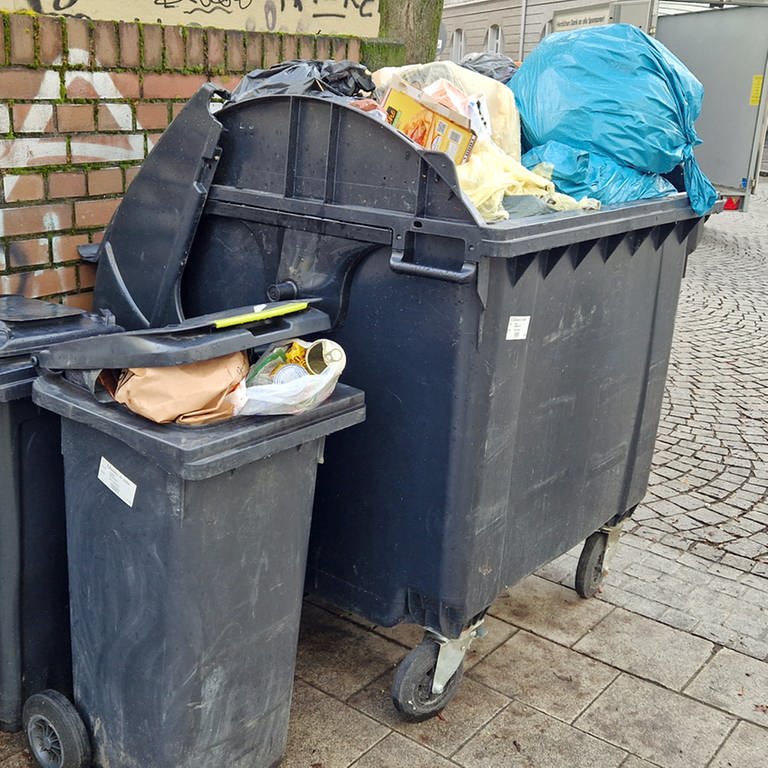 Mülltonnen stehen überfüllt an einer Hauswand