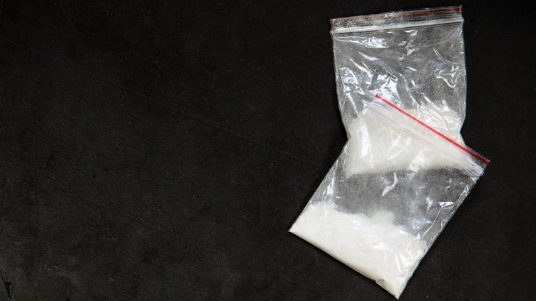 Zwei kleine Tütchen mit einem weißen Pulver vor schwarzem Hintergrund. Die Polizei in Ulm hat am Montag drei mutmaßliche Drogendealer gefasst.