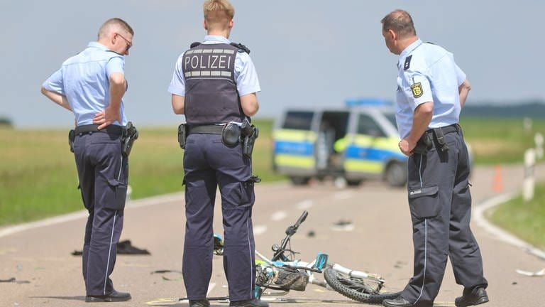 Polizisten schauen sich nach einem Unfall ein Kinderfahrrad auf der Straße an (Foto: z-media, Ralf Zwiebler)