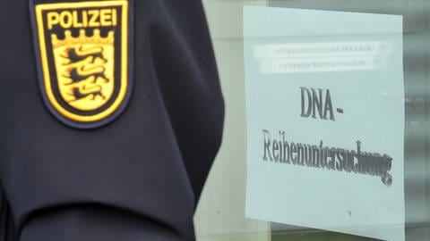 Polizeibeamter vor einer Tür mit der Aufschrift DNA-Reihenuntersuchung. Mit einem DNA-Reihentest versuchten die Ermittler im Mordfall Maria Bögerl dem Täter auf die Spur zu kommen (Archivbild).